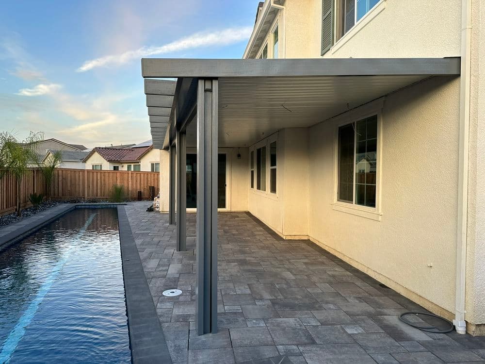 Modern patio with a pool, gray pergola, and spacious paved area in a residential backyard.